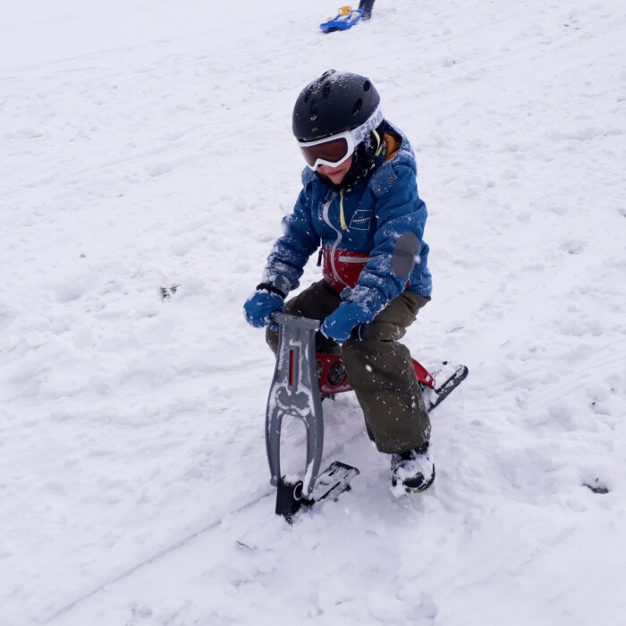 Kindergartenkind fährt mit dem Skibob mini auf der Rodelpiste