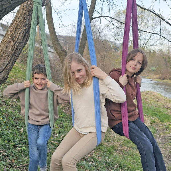 3 Kinder schaukeln in den neuen Erlebnistüchern der limited edition draußen am Baum