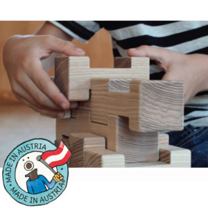 Kinderhände bauen einen Turm aus 4/4 Holzbausteinen. Daneben eine Grafik mit dem Text: Made in Austria.