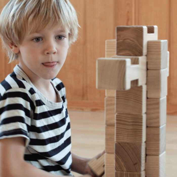 Kind baut hohen Turm aus 4/4 Holzbausteinen hergestellt in Österreich