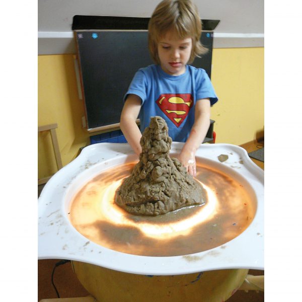Foto: Kind matscht mit Sand und Wasser im Wannenaufsatz auf einer beleuchteten Leuchttonne