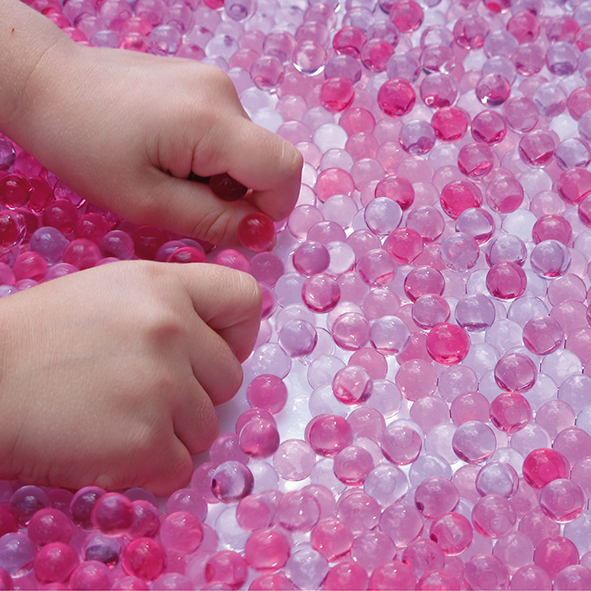 Kinderhände greifen in rosa gefärbte Wunderperlen.