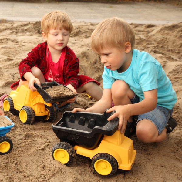 Foto: Kinder spielen mit großem Kipplaster in Sandkiste