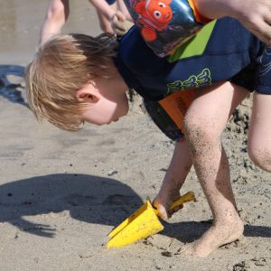 Foto: Kind gräbt mit gelber Sandschaufel im Sand