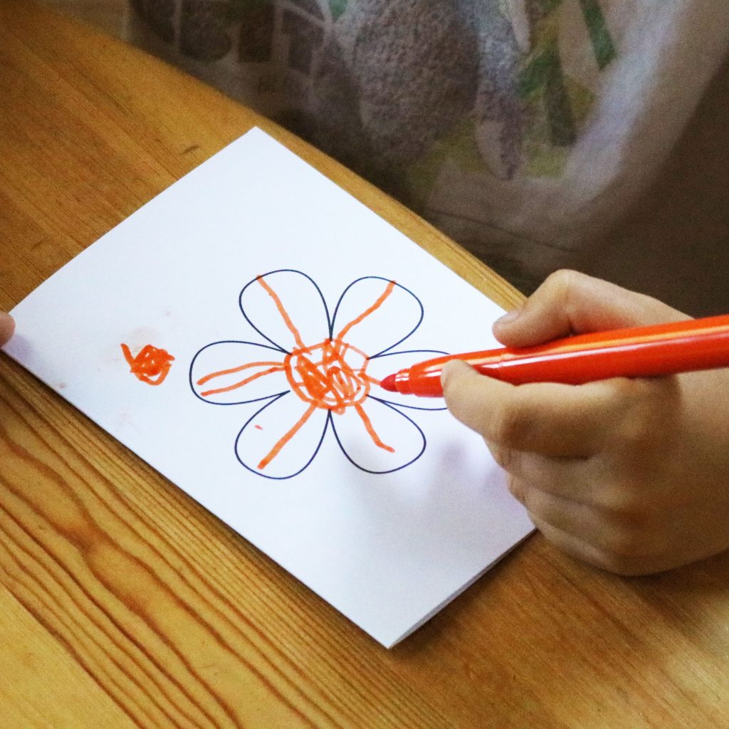 Foto: Kinderhand bemalt eine Grußkarte mit Blume