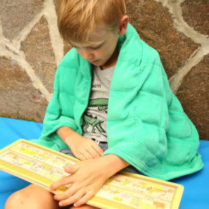 Kind liest mit Gewichtsdecke über der Schulter