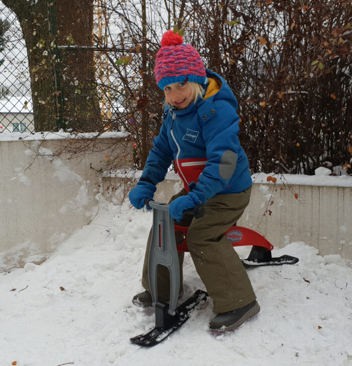 Kindergartenkind fährt mit dem Skibob mini im Garten