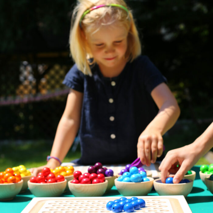 Kindergartenkind sortiert bunte Holzperlen in Materialschälchen aus Holz