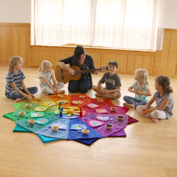 Farbenkreis mit Zubehör in Verwendung im Kindergarten als Jahreskreis. Pädagogin singt mit Kindern.