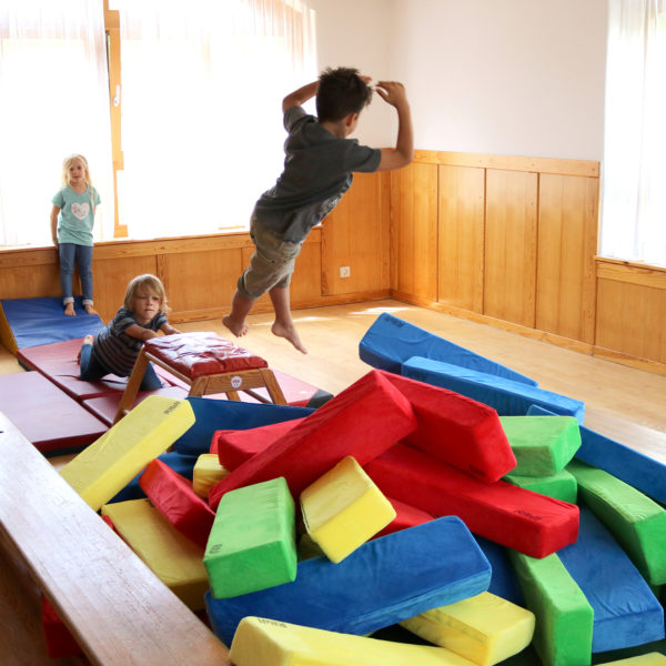 Kindergartenkinder springen im Turnsaal in eine Schitzelgrube aus RIWI Riesen-Softbausteinen