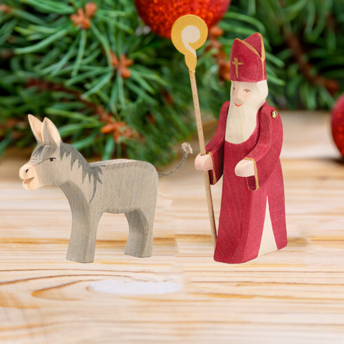 Holzfiguren Nikolaus und Esel für Kinder vor weihnachtlichem Hintergrund
