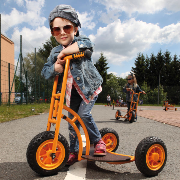 Kind im Kindergartenalter steht in cooler Pose mit Sonnenbrille auf dem robusten und sicheren Einstiegsroller Bengy von beleduc in orange