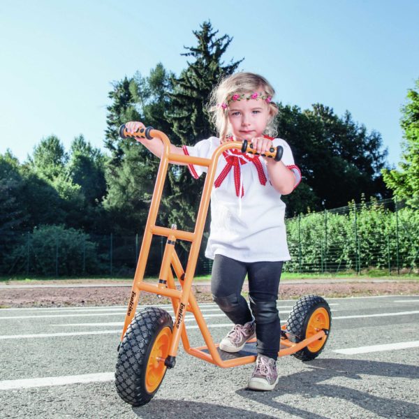 Mädchen im Kindergartenalter steht auf dem robusten und sicheren Roller Scooter klein von beleduc in orange