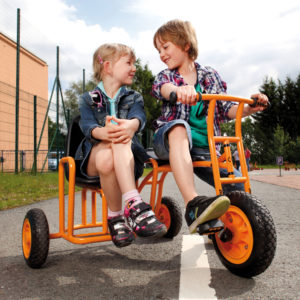Zwei Kinder im Kindergartenalter sitzen Seite an Seite auf dem Dreirad Seitenwagen von beleduc