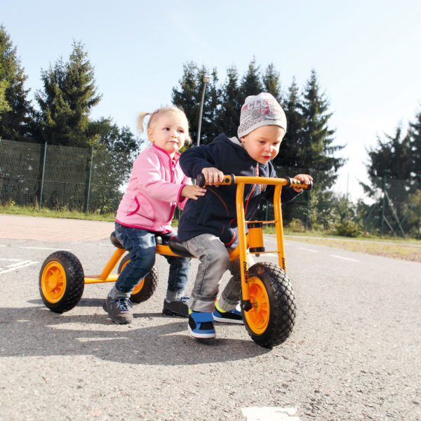 Zwei Kinder im Kindergartenalter fahren gemeinsam mit dem Laufrad Tandem wodurch die Koordination und das soziale Miteinander geschult werden.
