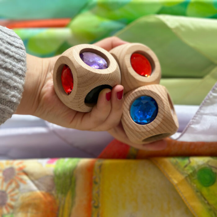 Eine Hand hält drei große Holzwürfel mit Glitzersteinen für Kinder