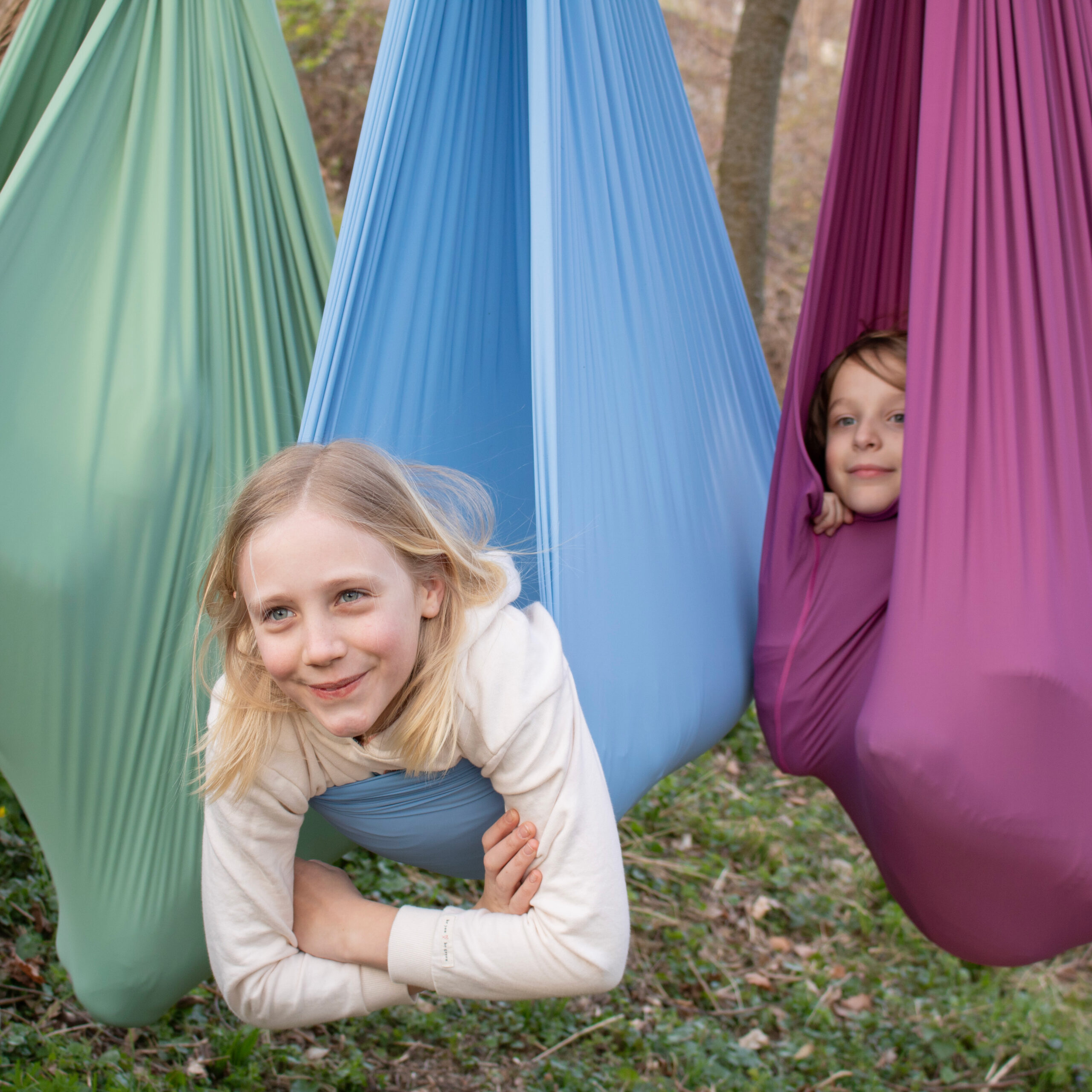 Drei Kinder schaukeln entspannt in den Erlebnistüchern in grün, hellblau und lila.